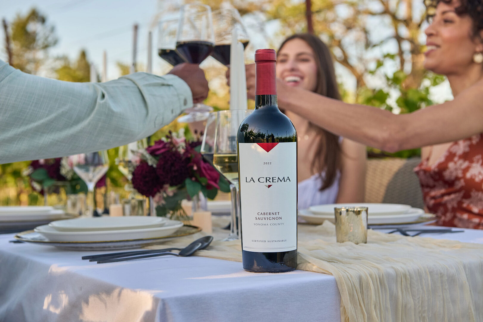La Crema Wine Bottles with glasses of wine and a plant in the background. 
